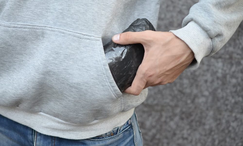 Drug dealer taking bag with cocaine out of hoodie pocket on dark tiles background close up Drug dealer taking bag with cocaine out of hoodie pocket on dark tiles background close up. Narcotic trafficking concept. Drug addiction